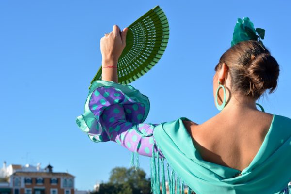 The woman with green flamenco dress is sheltered from the sun with the fan